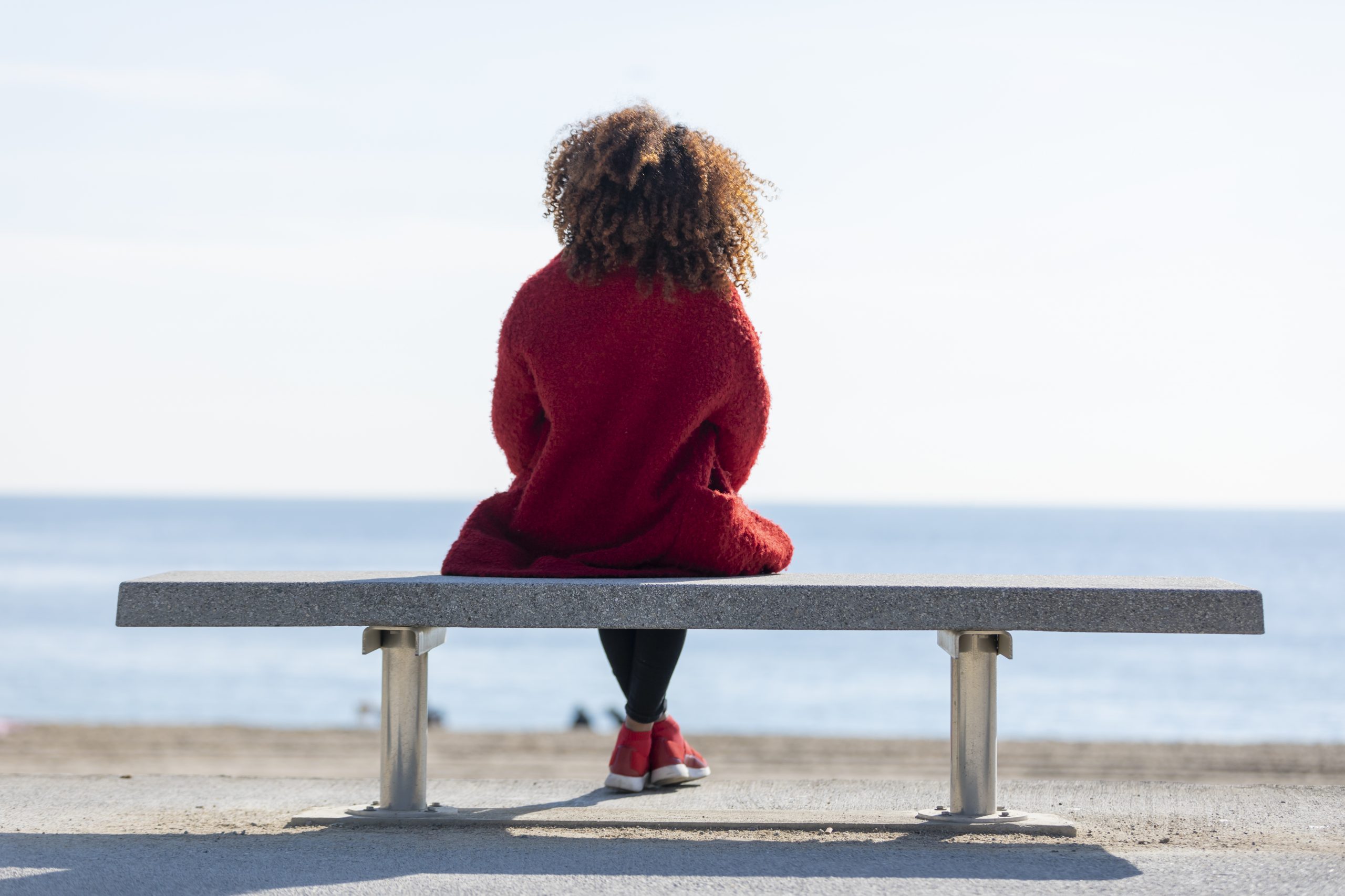 Thoughtful woman contemplating pregnancy options while sitting on a bench by a serene beach, reflecting on choices like abortion, adoption, or parenting.